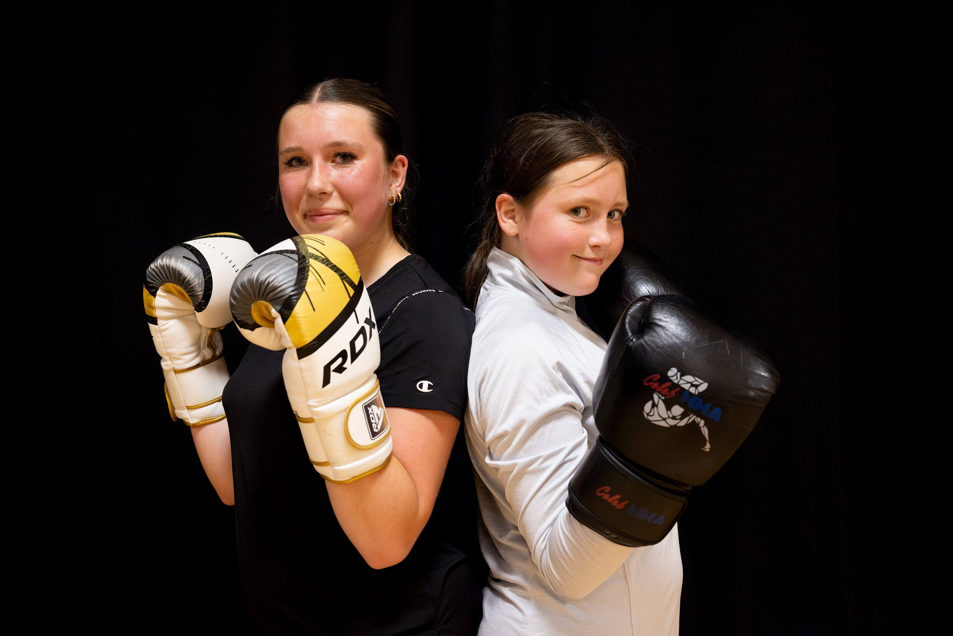 2 girls standing back to back with boxing gloves on.