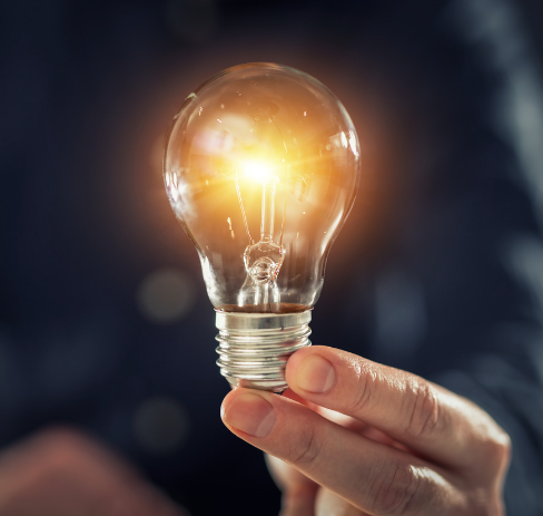 A person holding up a lit lightbulb